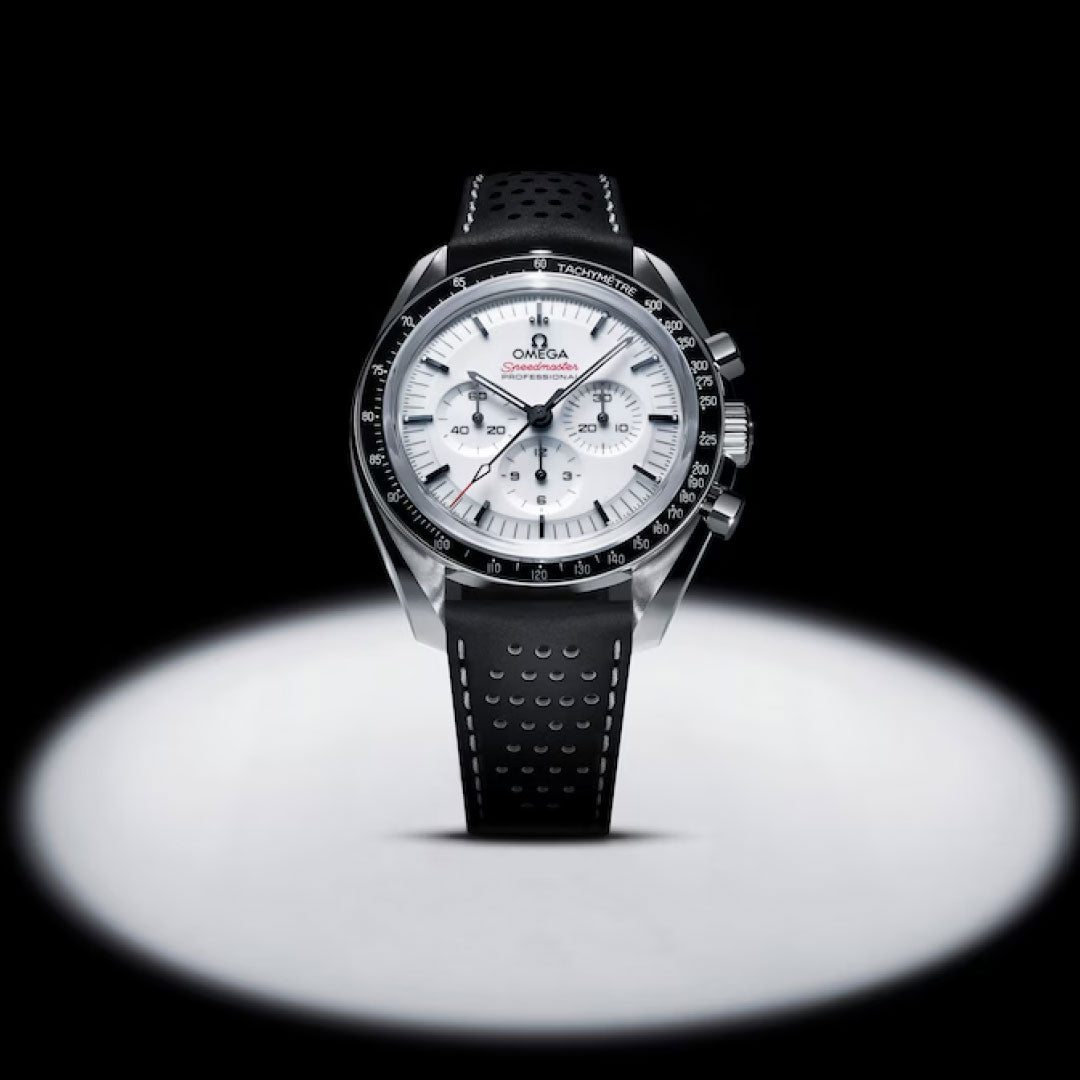 The OMEGA Speedmaster Moonwatch Professional Co-Axial Master Chronometer Chronograph 42mm stands upright in a spotlight, its white dial, black tachymeter bezel, and perforated strap showcased against a dark background—a true icon for chronograph fans.