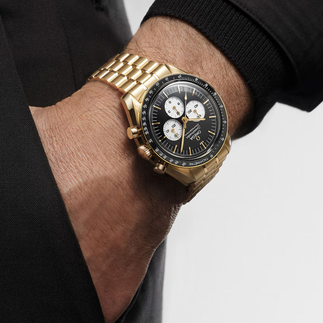 A close-up of a wrist wearing the OMEGA Speedmaster Moonwatch Professional Co-Axial Master Chronometer Chronograph 42mm with a black dial and three white subdials, paired with a dark long-sleeve garment.