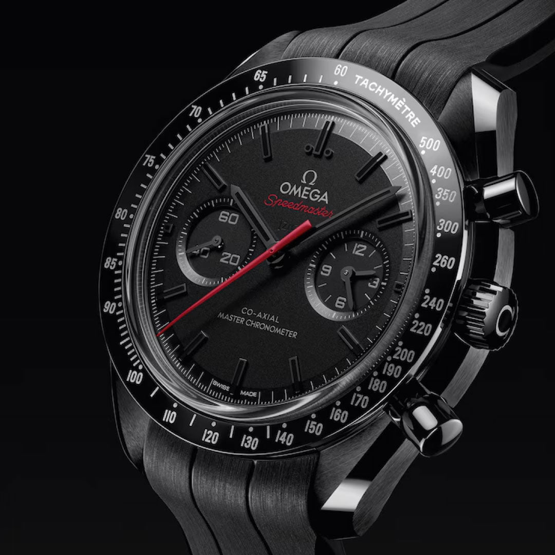 A close-up of the OMEGA Speedmaster Dark Side of the Moon Co-Axial Master Chronometer 44.25mm watch featuring a black ceramic case, tachymeter bezel, two subdials, red second hand, and textured black strap against a dark background.