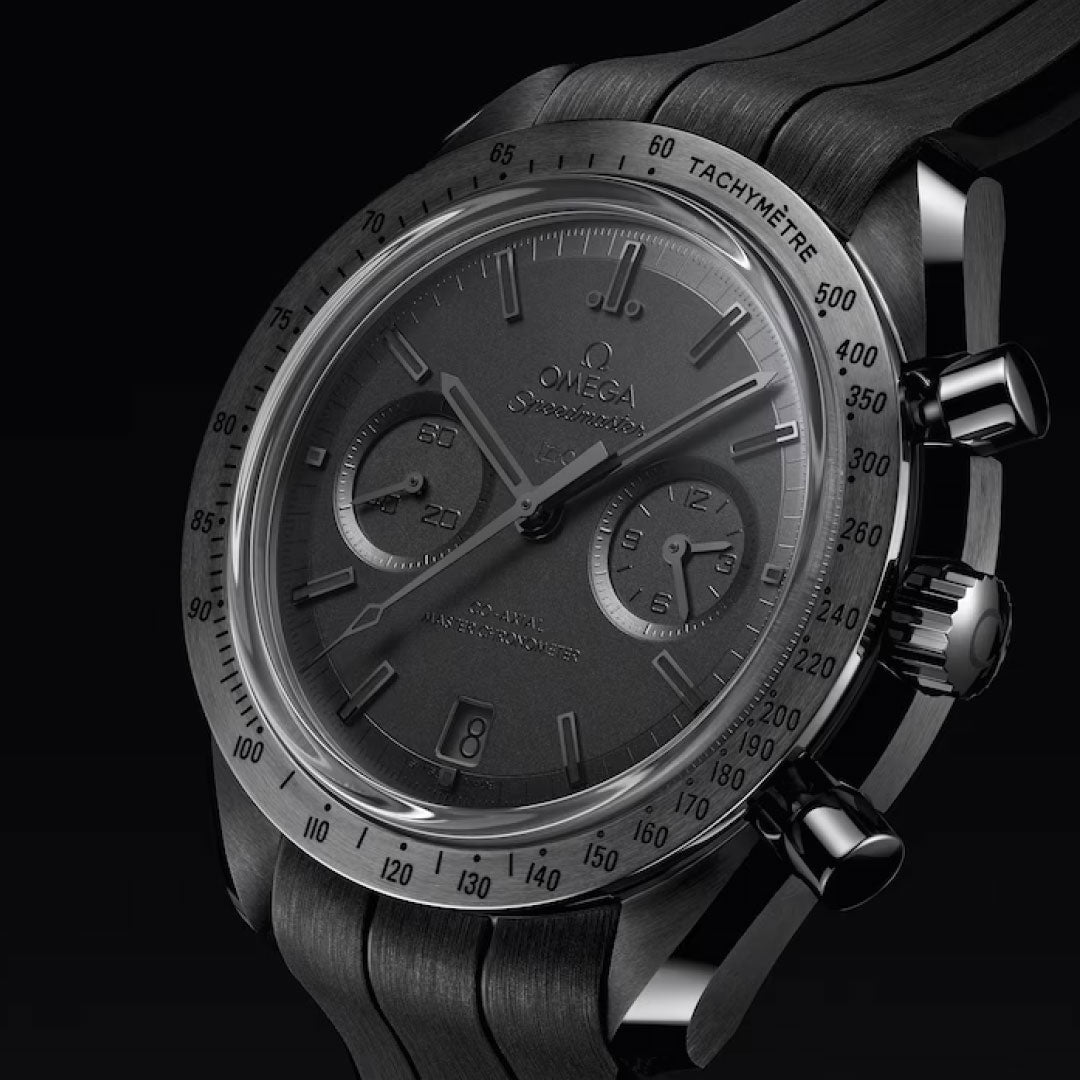 A close-up of the OMEGA Speedmaster Dark Side of the Moon Co-Axial Master Chronometer 44.25mm showcases its black ceramic case, black dial with chronograph subdials, tachymeter bezel, and metal pushers against a black background.