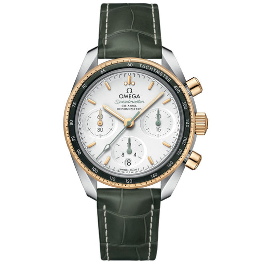 The OMEGA Speedmaster 38 Co-Axial Chronometer Chronograph 38mm Watch features a green leather strap and a silver-gold case. It presents a white dial adorned with three subdials, gold accents, and the renowned OMEGA Co-Axial Calibre 3330 movement. The tachymeter scale on the bezel enhances this classic design, with the "Omega" logo prominently displayed on the dial.