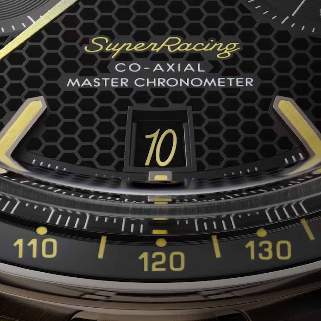 A detailed view of the OMEGA Speedmaster Super Racing Co-Axial Master Chronometer 44.25mm watch reveals a black watch face adorned with a hexagonal pattern. The terms "SuperRacing" and "Speedmaster" are prominently displayed, highlighting its precision as a Co-Axial Master Chronometer. The date window displays the number "10." The design is presented in a striking yellow and black color scheme with elegant gold accents.