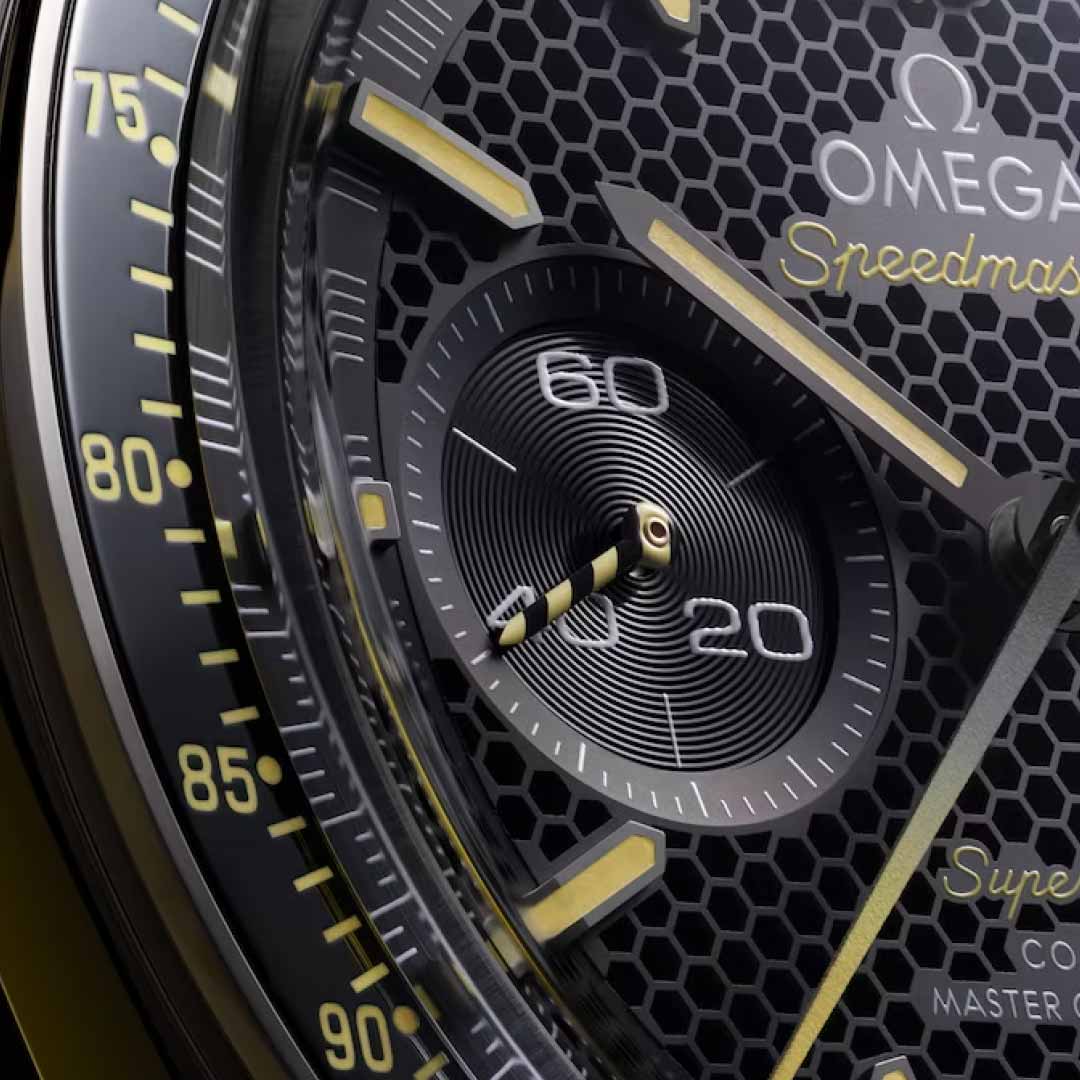 Close-up of the OMEGA Speedmaster Super Racing Co-Axial Master Chronometer 44.25mm watch face showcasing a textured honeycomb design. It features gold accents, luminescent hands, and a sub-dial marked with "60" at the top. The words "OMEGA Speedmaster" are elegantly inscribed on the dial, highlighting its advanced Co-Axial Master Chronometer technology.