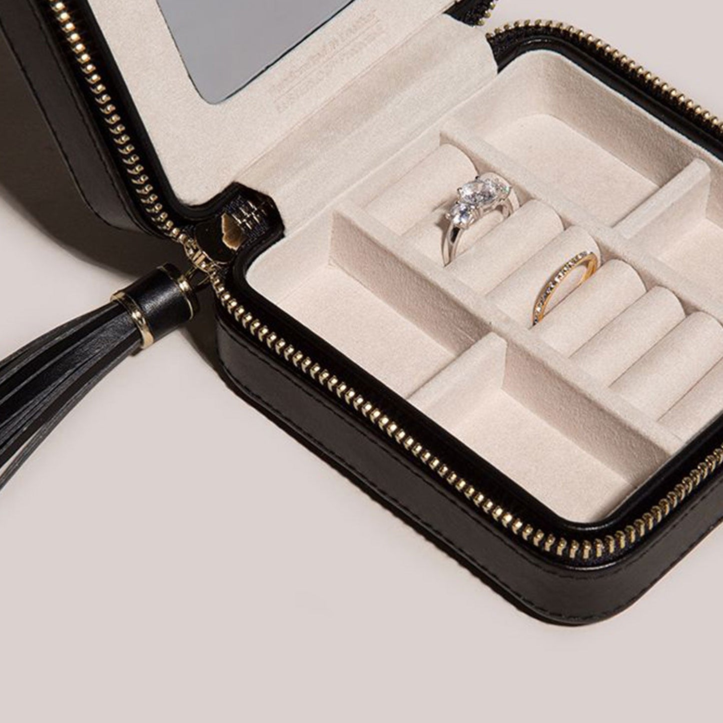 The WOLF 1834 Caroline Zip Travel Case by WOLF is a compact black jewelry case featuring a zipper closure and cushioned compartments that help prevent tarnish. Inside, you'll find an engagement ring with a large stone and a wedding band, and the case comes with an attached black tassel, making it ideal for traveling with your jewelry.