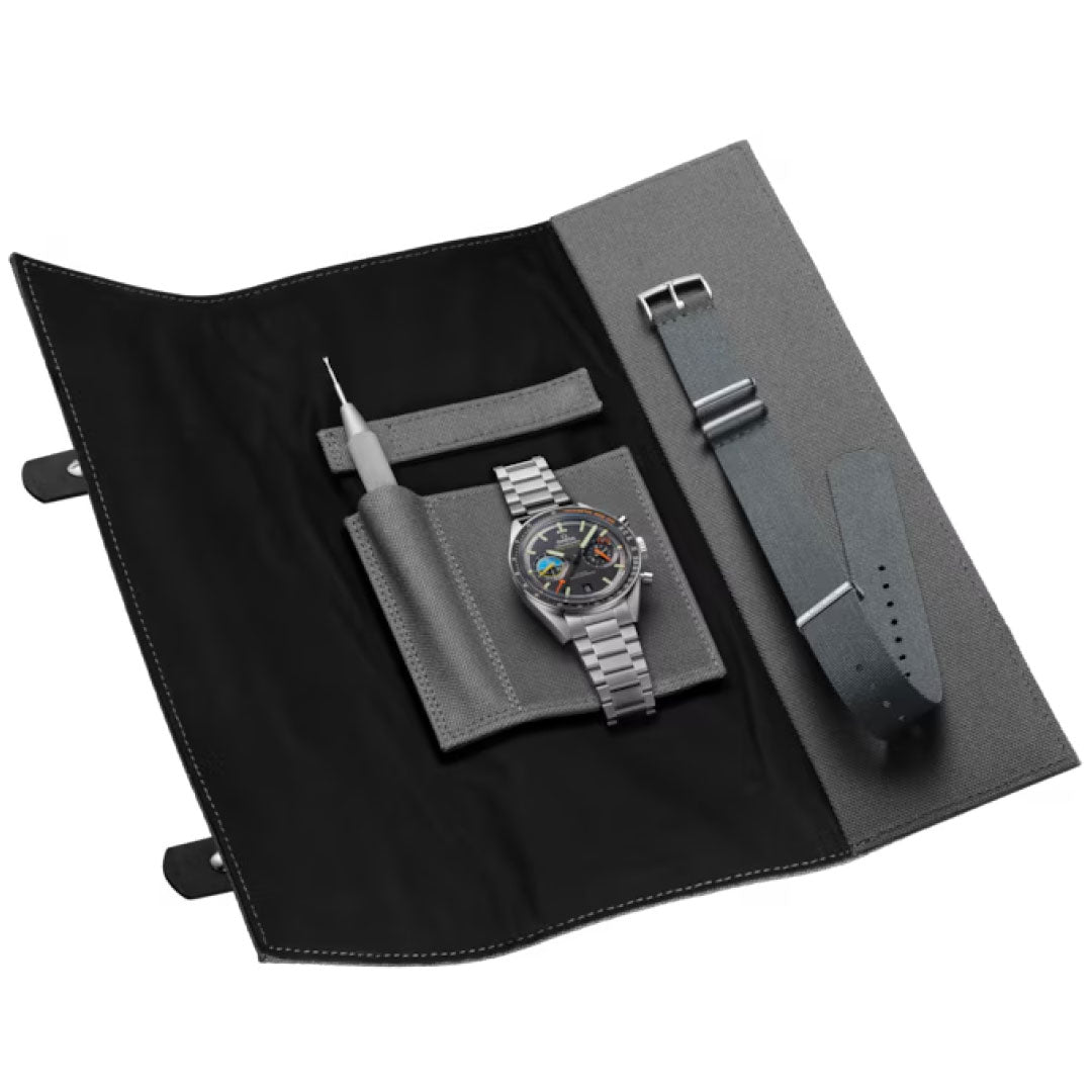 A grey fabric watch roll reveals an OMEGA Speedmaster Pilot Co-Axial Master Chronometer 40.85mm Watch, a metal band, leather strap, clasp, and tool—all neatly arranged in compartments, reflecting OMEGA's moon landing and flight heritage.