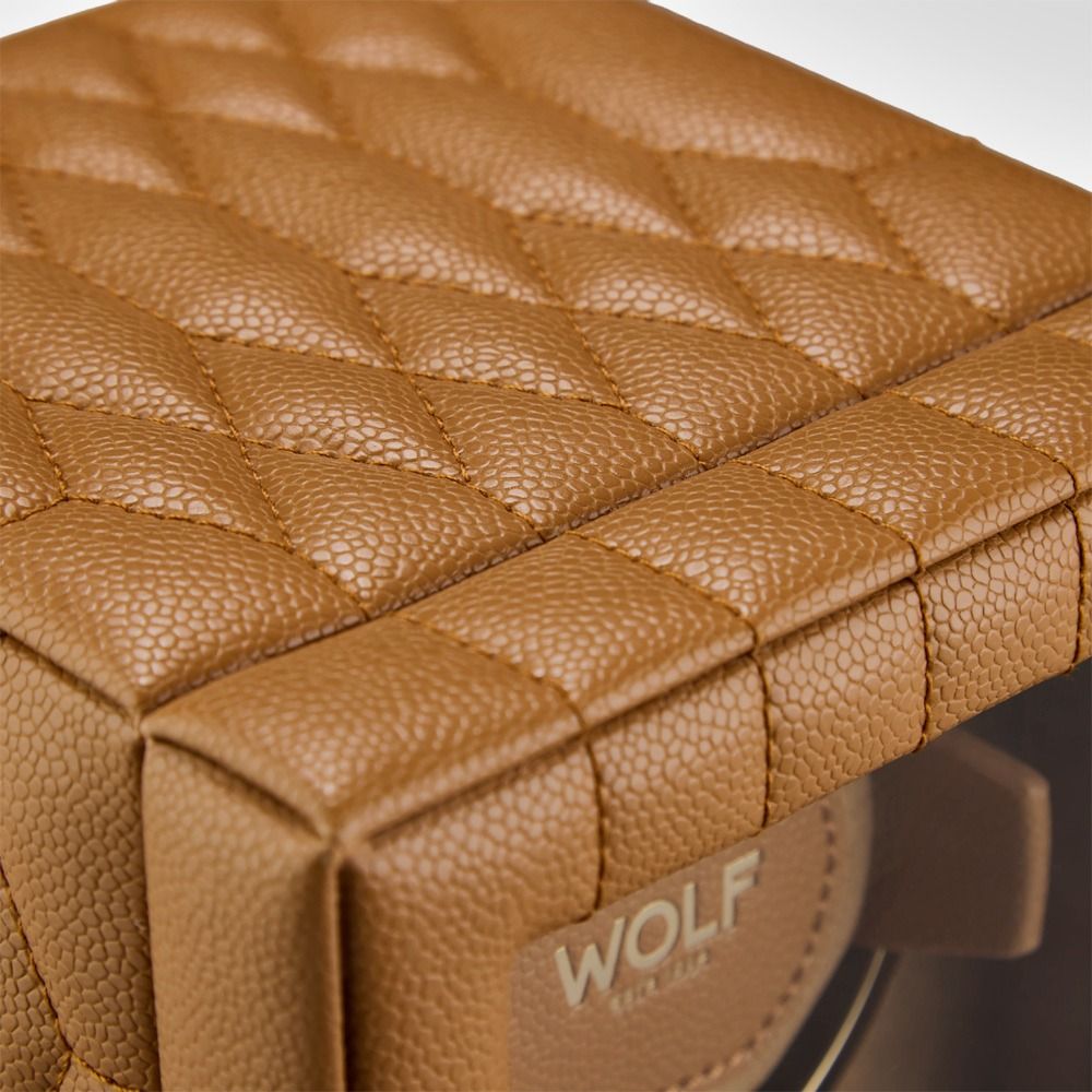 Here’s a rewritten version of the sentence using your product data: Close-up of the WOLF 1834 Lauren Single Watch Winder Carmel—a brown, textured, quilted leather box with the “WOLF” brand name partially visible through a transparent window. This elegant piece features subtle British roadster-inspired details for a timeless touch.