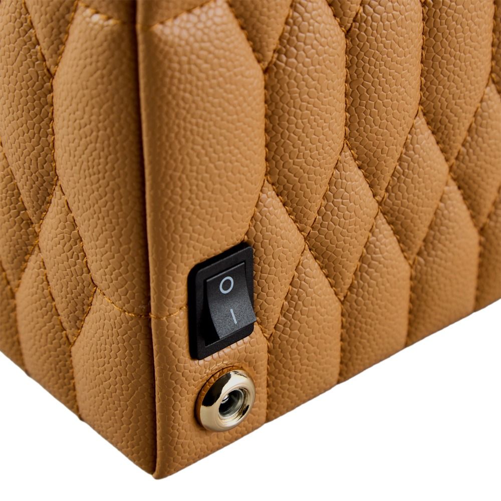 A close-up of the WOLF 1834 Lauren Single Watch Winder Carmel showcases its brown, quilted, textured surface, featuring a black on/off switch and a circular metal grommet—design elements inspired by British roadsters and commonly found in luxury watch winder cases from WOLF.