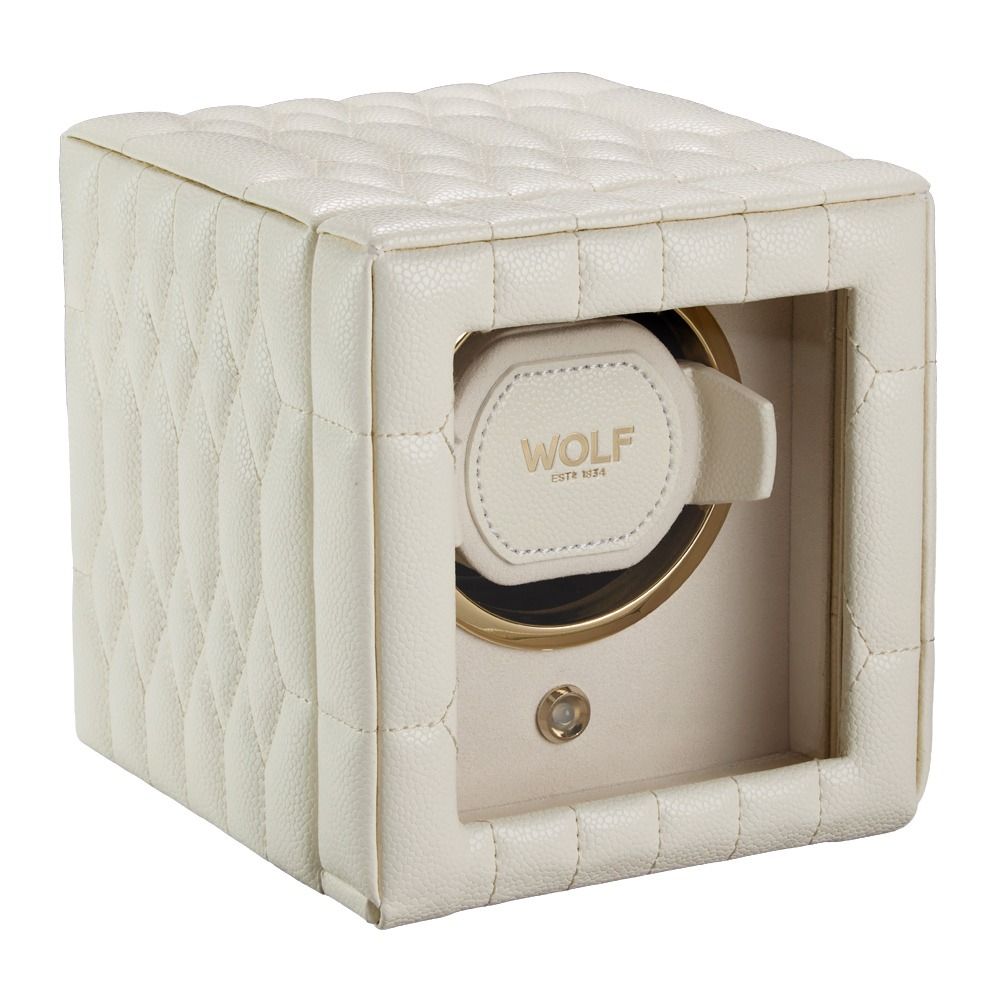 The WOLF 1834 Lauren Single Watch Winder Ivory features a cream-colored, quilted design with a glass front, sleek chrome hardware, and elegant ebony macassar wood trim. Inside, it includes a padded holder labeled “WOLF Est. 1834.”.