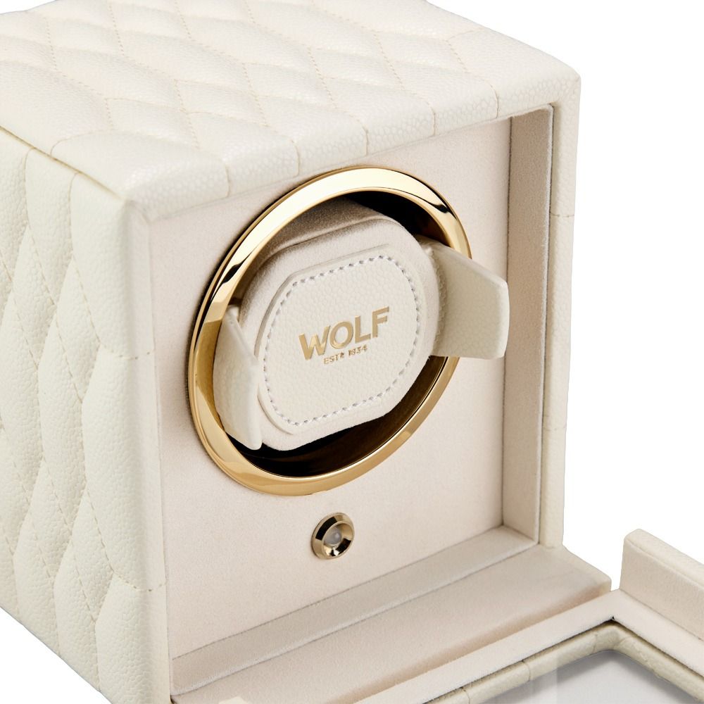 The WOLF 1834 Lauren Single Watch Winder in Ivory by WOLF features a cream-colored, quilted exterior with elegant gold accents and “WOLF EST. 1834” printed inside. The partially open winder reveals its plush interior, chrome hardware, and the circular mechanism designed to securely hold your watch.