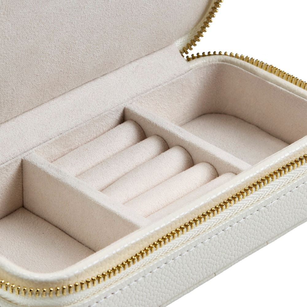 A close-up of an open, ivory leather jewelry case with a zipper reveals compartments and cushioned ring holders inside. The WOLF 1834 Lauren Med Jewellery Box Ivory by WOLF offers elegant, anti-tarnish storage for your precious accessories.
