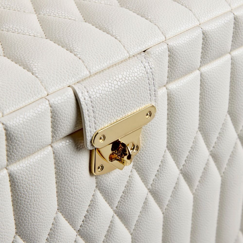 Close-up of the WOLF 1834 Lauren Med Jewellery Box Ivory, a quilted white leather jewelry box by WOLF featuring a gold-tone clasp on the front. The textured, patterned leather surface and visible stitching provide a luxurious and elegant appearance, while offering anti-tarnish storage to keep your valuables safe.