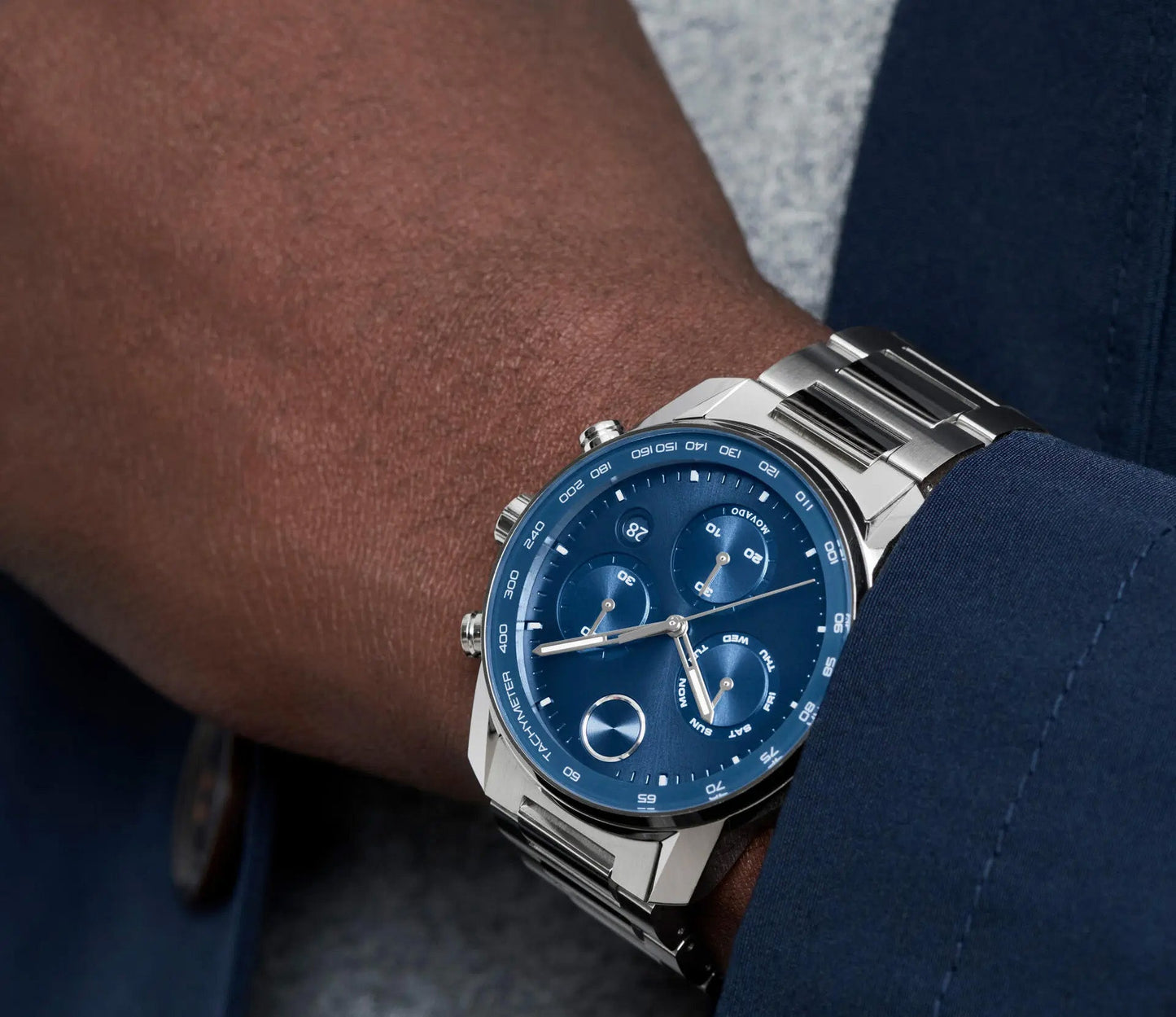 A close-up of a person wearing the sophisticated Movado BOLD Verso Quartz 44mm Watch, which showcases a blue dial encased in elegant silver. The stainless steel case is complemented by a metal bracelet, and the person is dressed in an elegant dark blue suit.