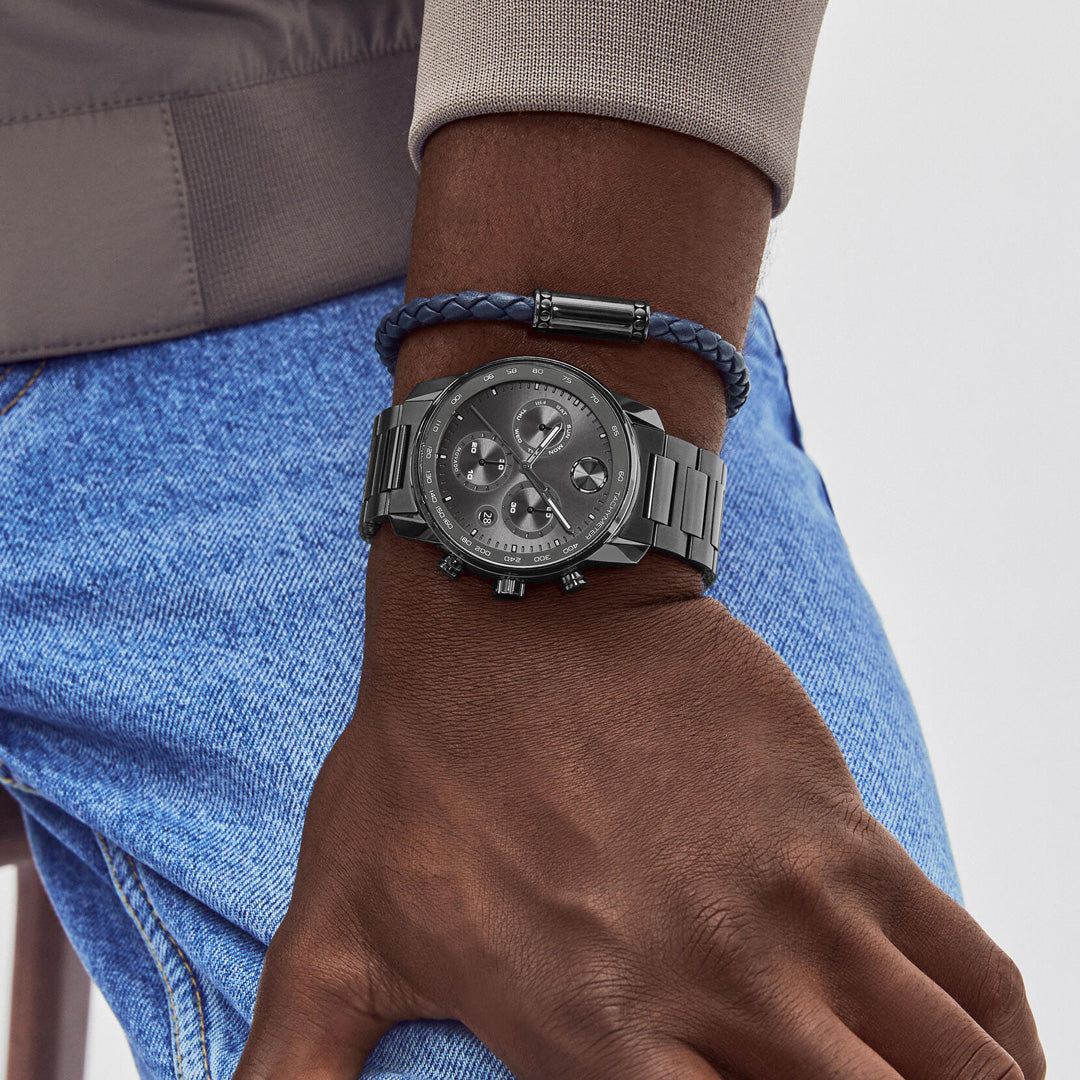 A person wearing blue jeans and a beige jacket showcases the Movado BOLD Verso Chronograph Quartz 44mm Watch with a tachymeter bezel and a braided navy bracelet on their left wrist. Their hand rests relaxed by their side.
