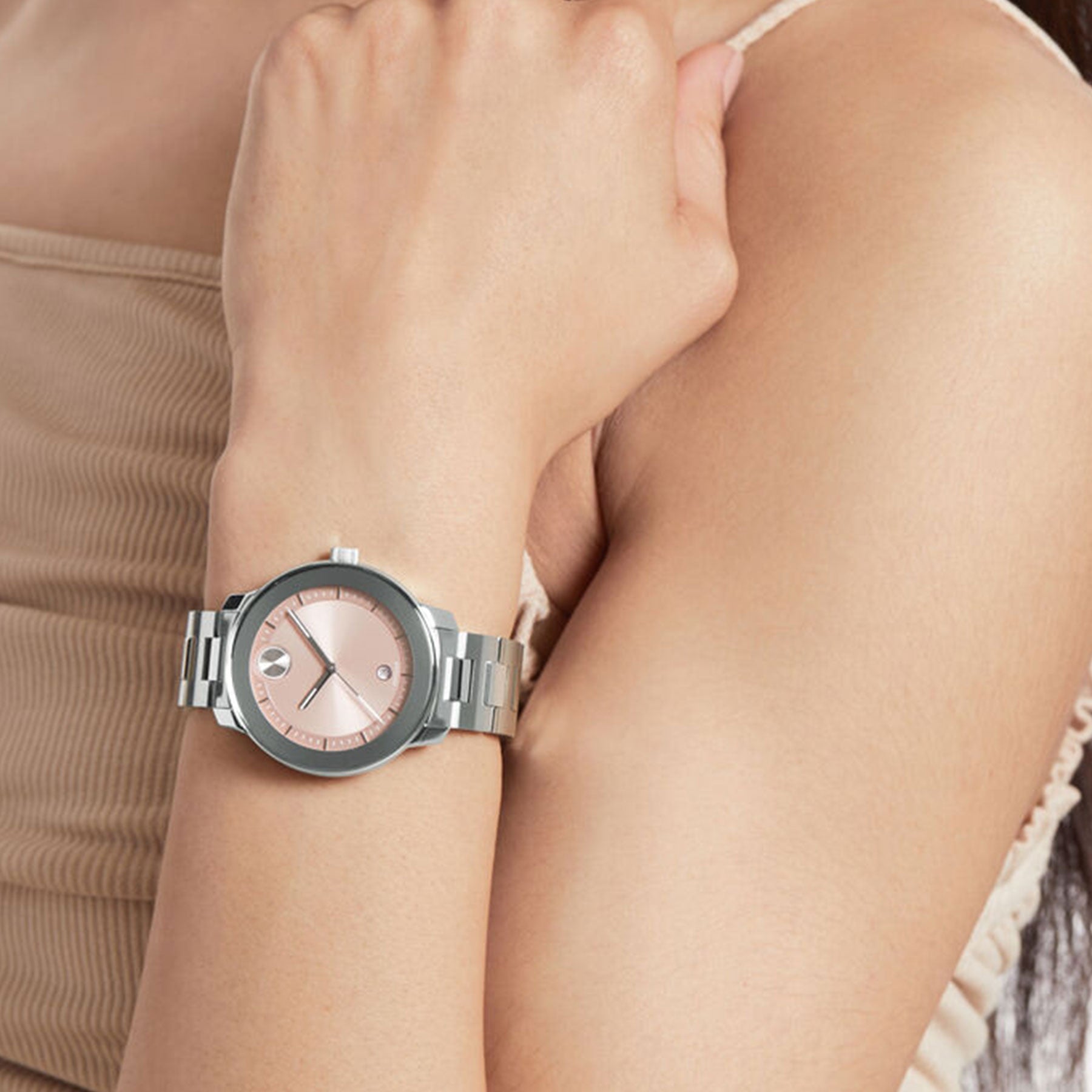 A person in a sleeveless beige top showcases the Movado BOLD Verso Quartz 38mm Watch, featuring a blush dial and metallic band. The left arm is bent, resting across the waist.