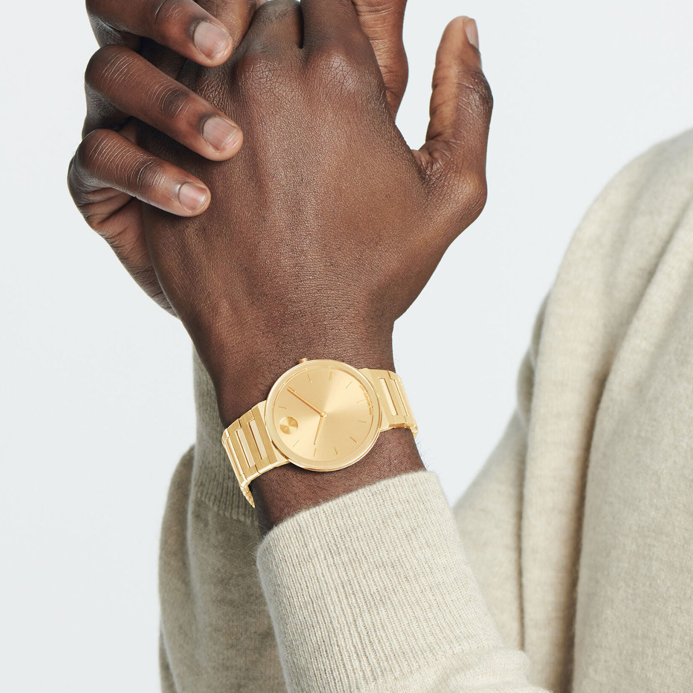 A person wearing a light sweater showcases the Movado BOLD Horizon Quartz 40mm Watch, featuring a gold round face and minimalist design. The metallic watchband enhances its elegant, modern look against the neutral background.