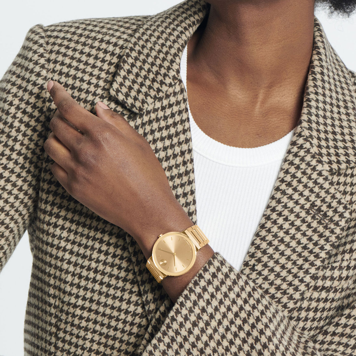 A person in a brown houndstooth blazer and white shirt showcases the Movado BOLD Horizon Quartz 40mm Watch, featuring a classic round face. The hand is elegantly positioned near the blazer's collar against a plain white backdrop.