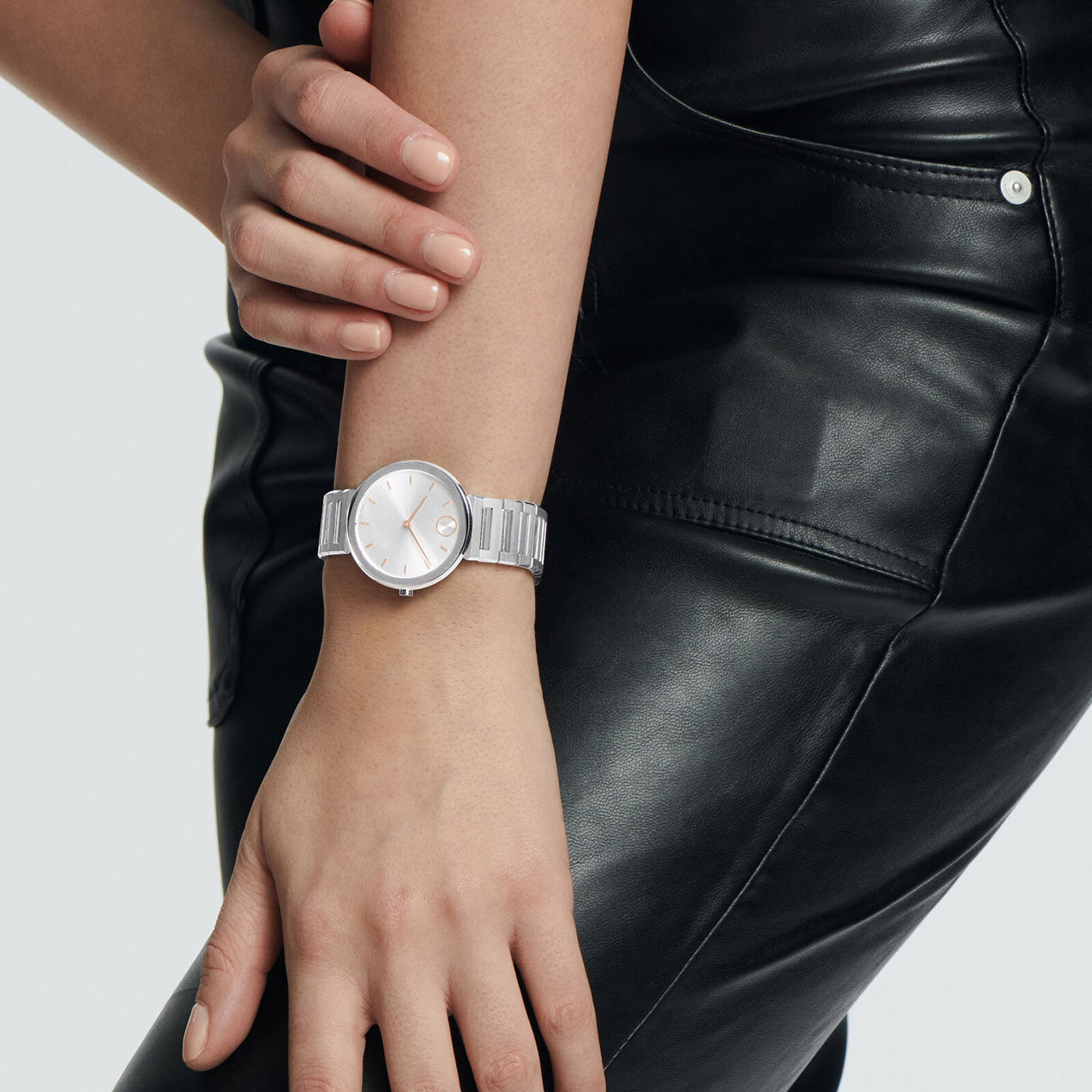 A person is sporting a Movado BOLD Horizon Quartz 34mm Watch, featuring a minimalist and shiny silver design with a round dial. Dressed in a sleek black leather outfit, only the watch and part of the clothing stand out against a simple background.