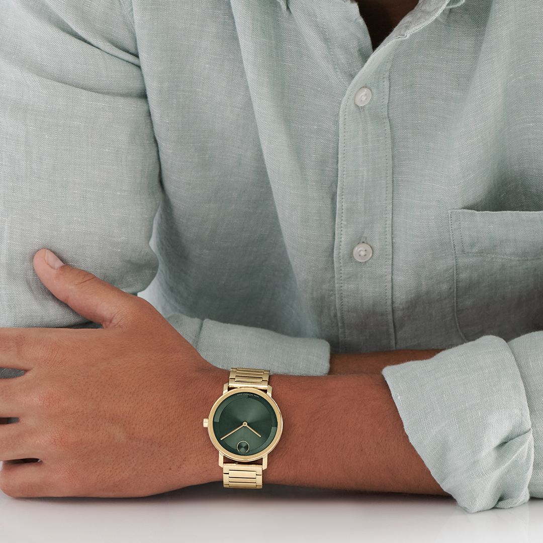 A person wearing a Movado BOLD Evolution 2.0 Quartz 40mm Watch with a yellow gold-tone finish and a dark green dial on their wrist.