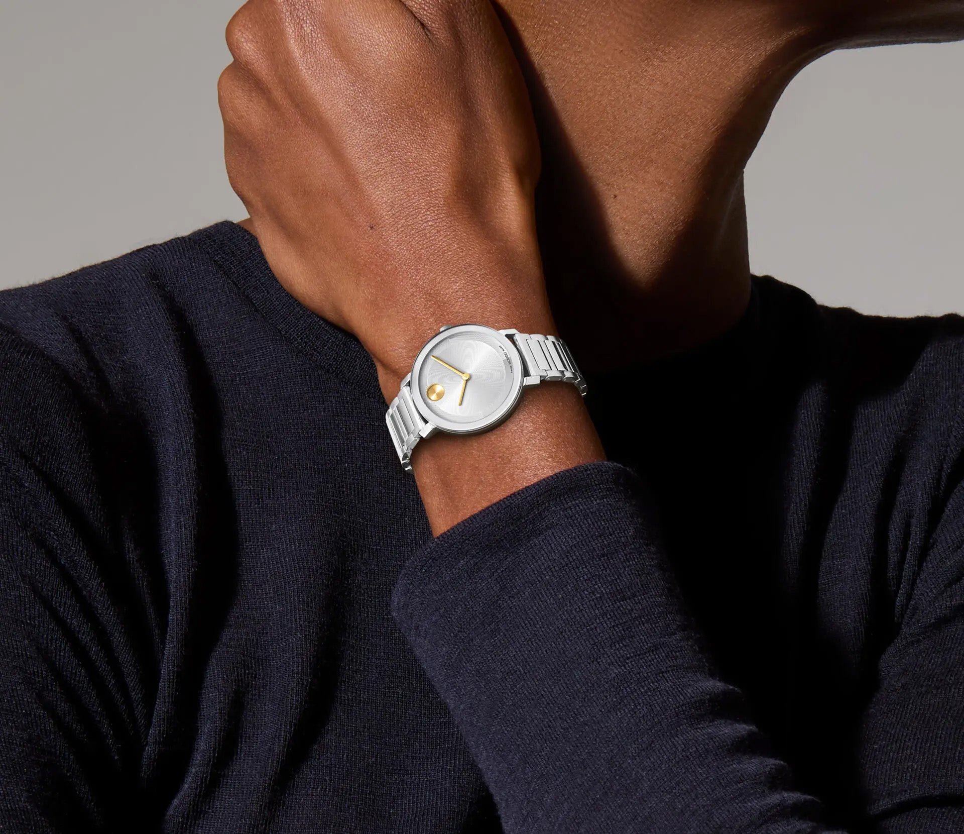 A person wearing a dark long-sleeve shirt models a contemporary silver wristwatch with a micro-textured dial. The timepiece, the Movado BOLD Evolution 2.0 Quartz 34mm Watch, features a silvertone lacquer dial and a sleek metal link bracelet. With the arm bent, it highlights the minimalist design of this Movado piece in full view, perfectly embodying the BOLD Evolution 2.0 style.