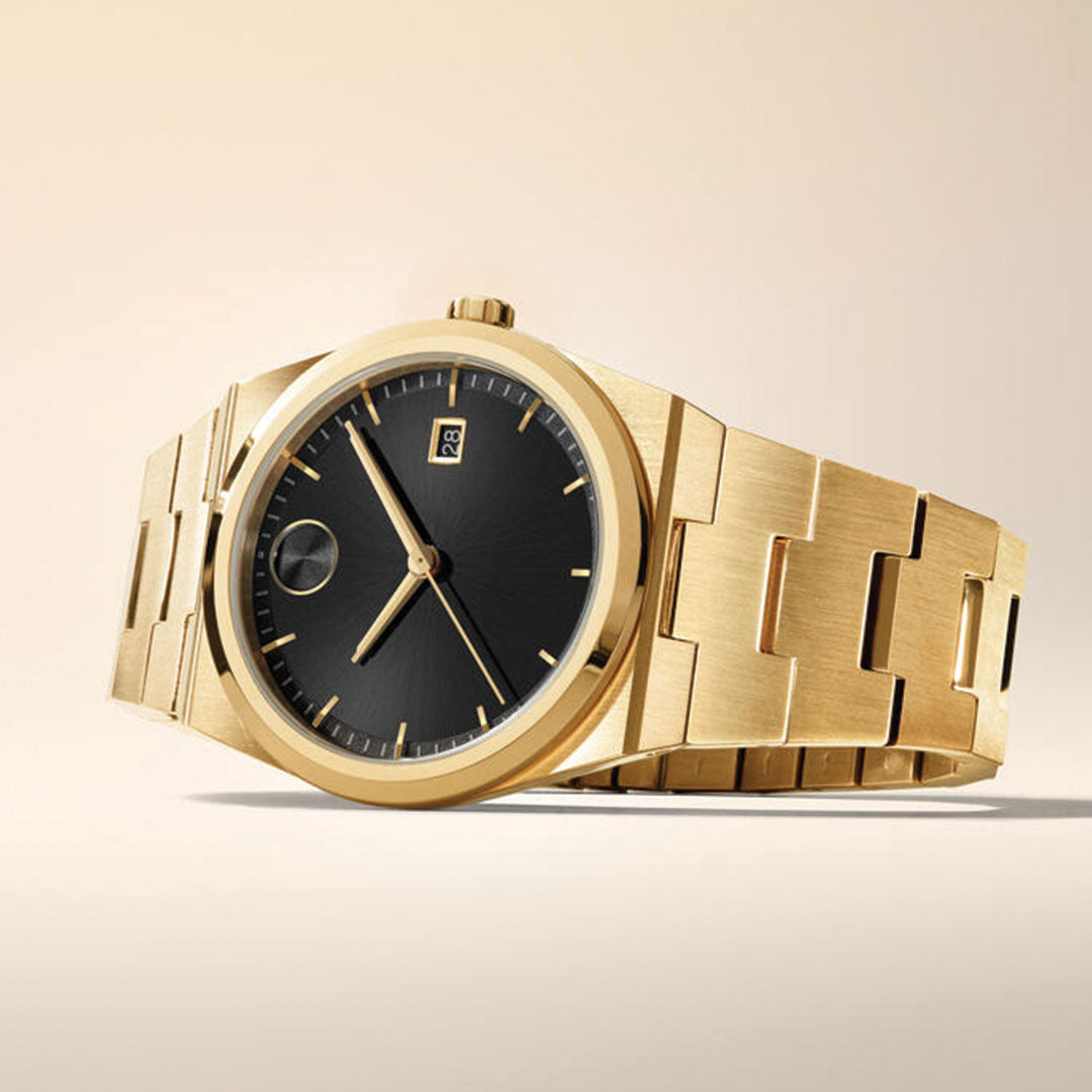 The Movado BOLD Quest Quartz 40mm Watch, featuring a gold case, black sunray dial, gold hour markers, and date display, is showcased on a light surface with its chunky polished bracelet contrasting the beige background.