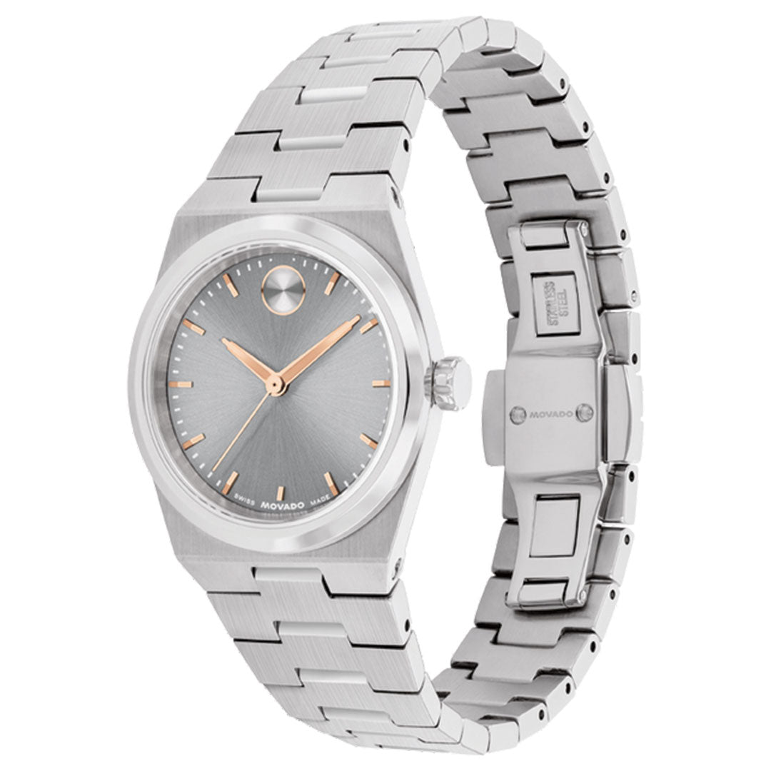 The Movado BOLD Quest Mini Quartz 28mm Watch features a silver brushed metal link band, minimalist gray dial, gold-tone hands, and signature dot at 12 o’clock. It’s shown angled to display the face and open clasp.