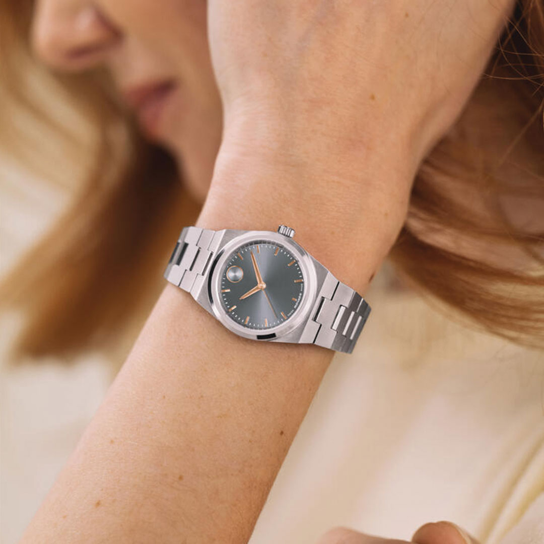 A woman wears the Movado BOLD Quest Mini Quartz 28mm watch, featuring a sleek silver and rose gold tone.