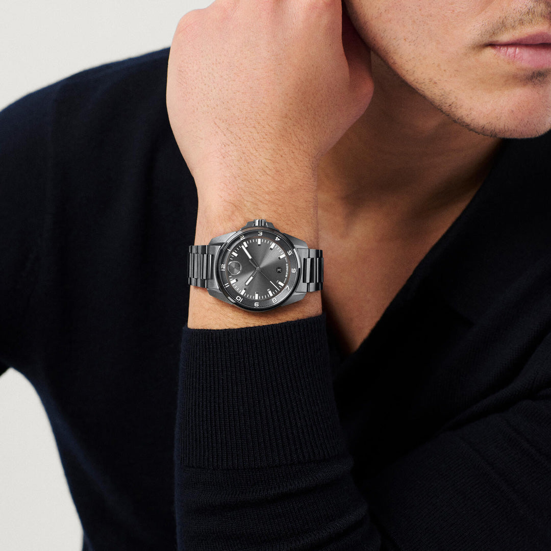 A person wearing a black long-sleeve shirt rests their chin on their hand, showcasing the Movado BOLD Verso S Quartz 42mm Watch by Movado, which features a silver case, black dial, and silver markers. Only the lower half of the face and upper torso are visible.