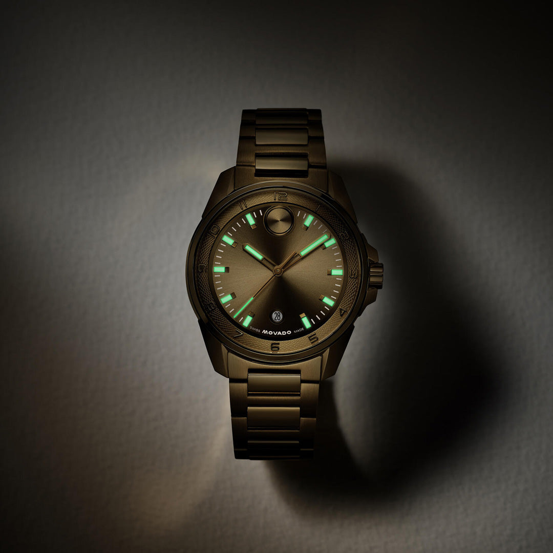 The Movado BOLD Verso S Quartz 42mm Watch by Movado, featuring a metallic design with a dark face and luminous green hour markers and hands, showcases its reliable Swiss made movement against a softly lit background.
