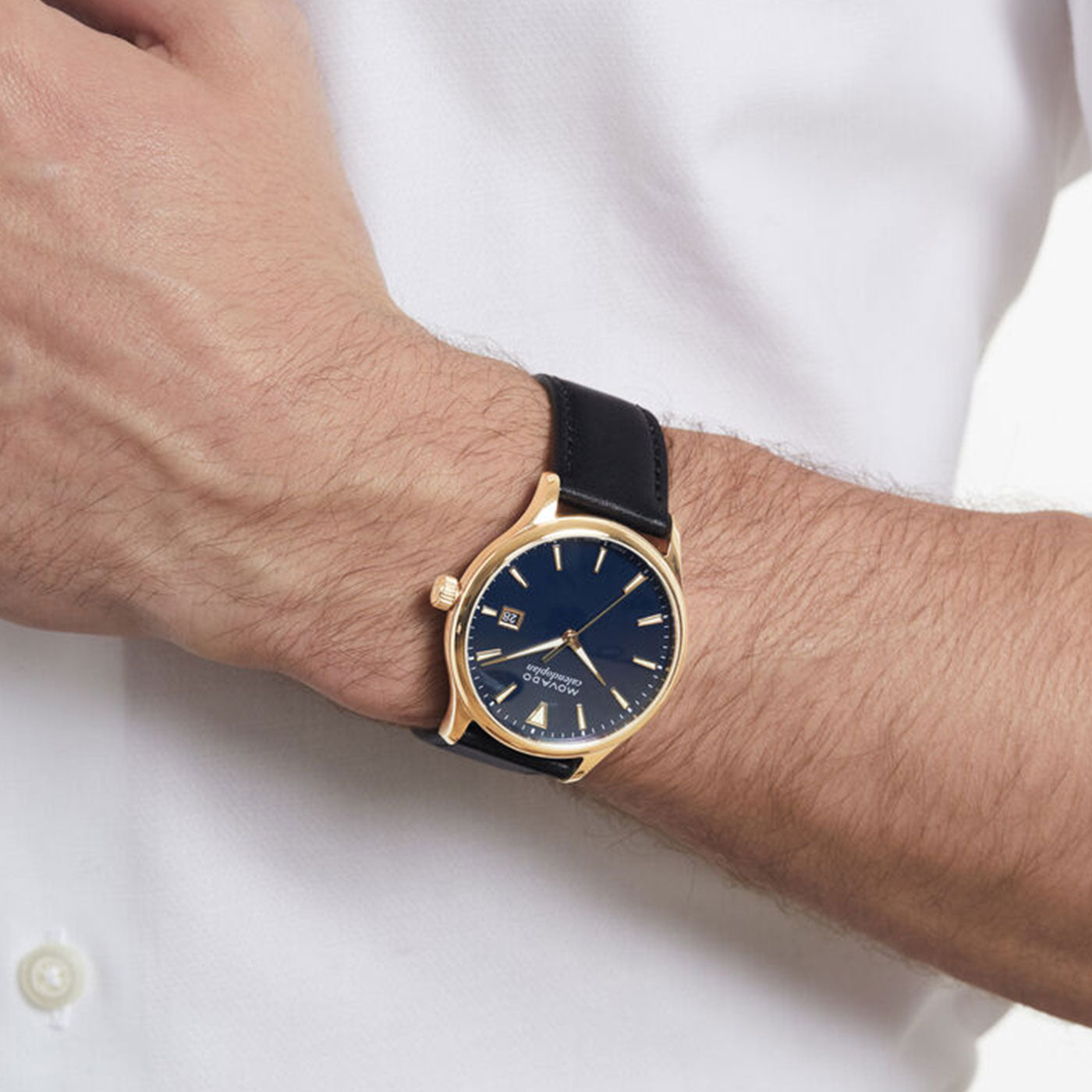 A person wearing a Movado Heritage Series Calendoplan Quartz 40mm Watch, which has a rose gold finish, black dial, and black leather strap. The watch includes a date display and Swiss Super-LumiNova® gold hour markers, perfectly complementing their white button-up shirt.