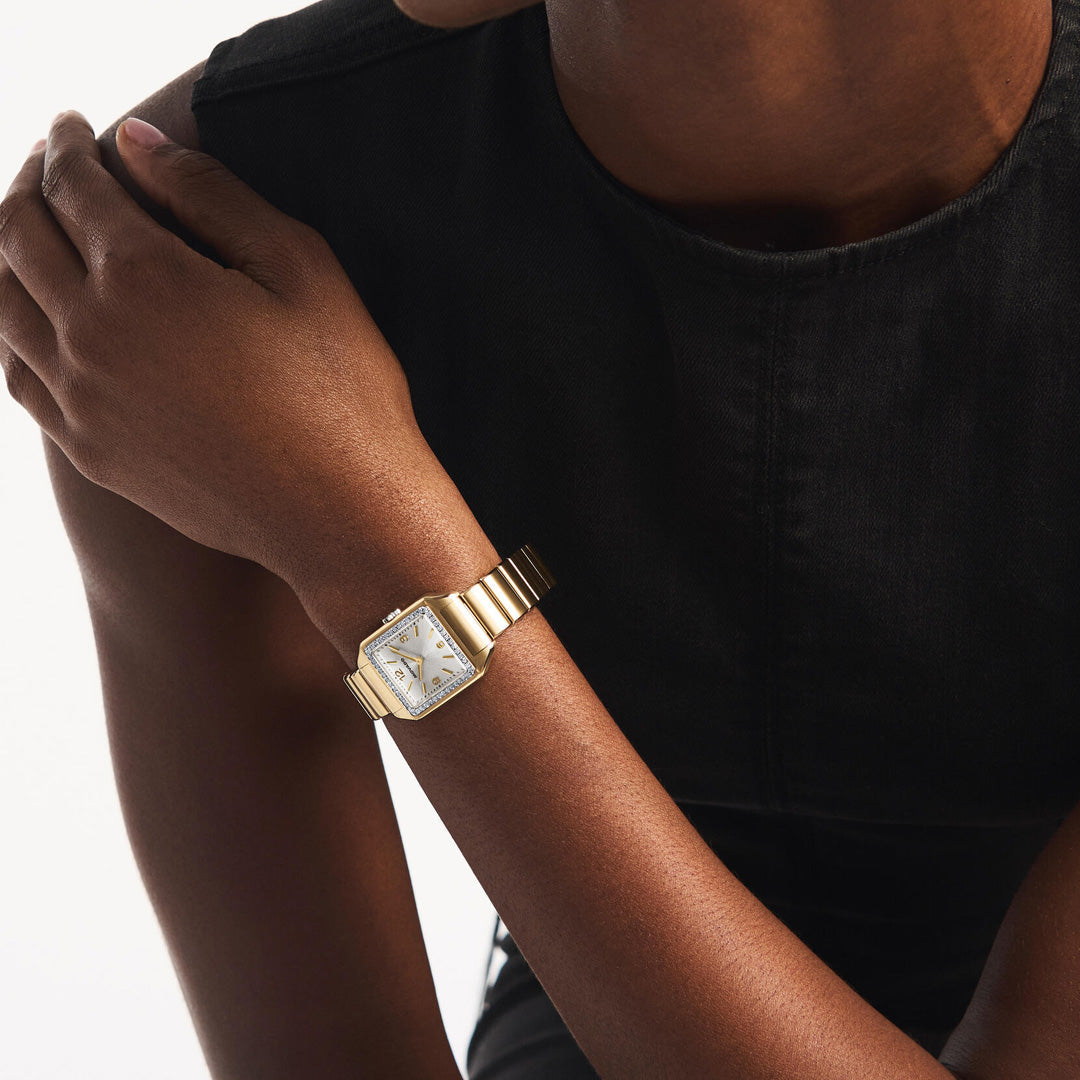 A person wearing a sleeveless black top rests their left arm on their right shoulder, showcasing the Movado Heritage 1917 Quartz 25mm x 34.10mm Watch by Movado, featuring a gold, lab-grown diamond bezel and a striking square face.