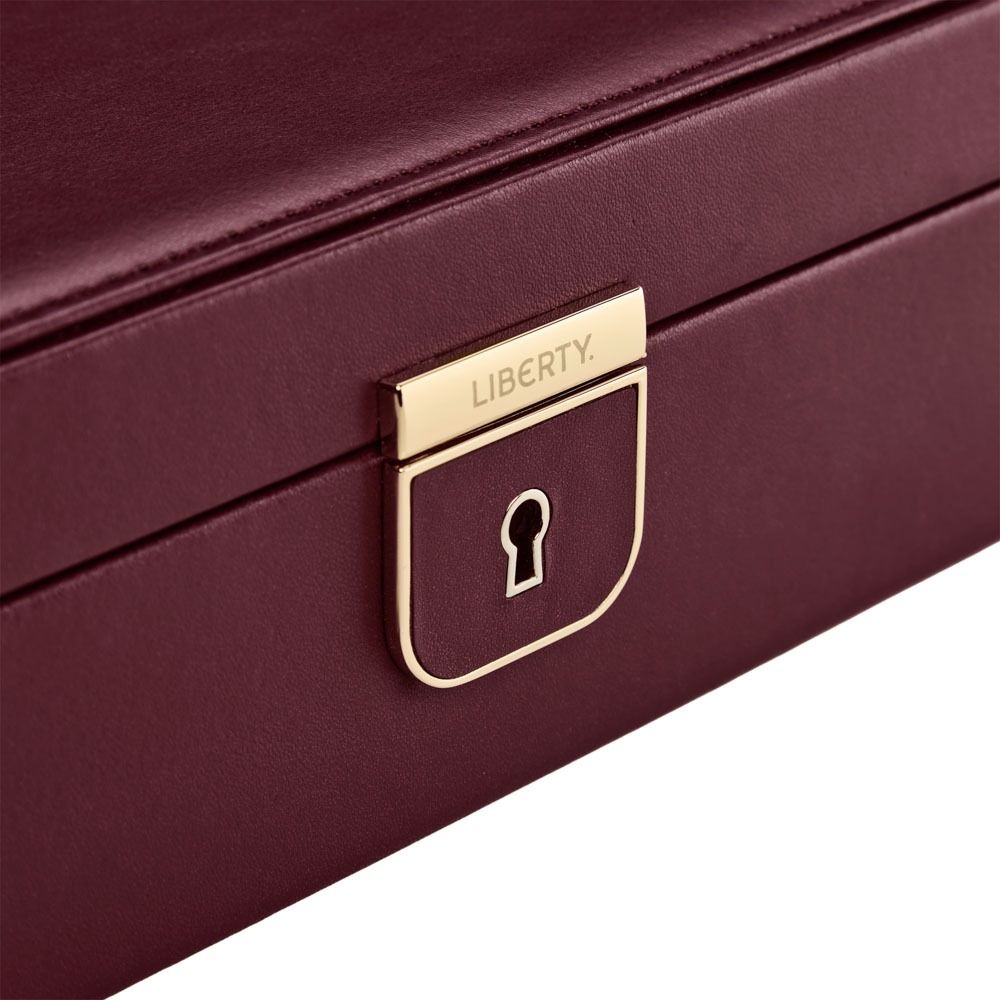 A close-up of the WOLF 1834 X Liberty All Over Ianthe Medium Jewellery Box in Burgundy, crafted from maroon lizard-embossed leather with smooth texture and clean edges. The jewellery box features a gold lock with a keyhole on the front, engraved with “WOLF.”.
