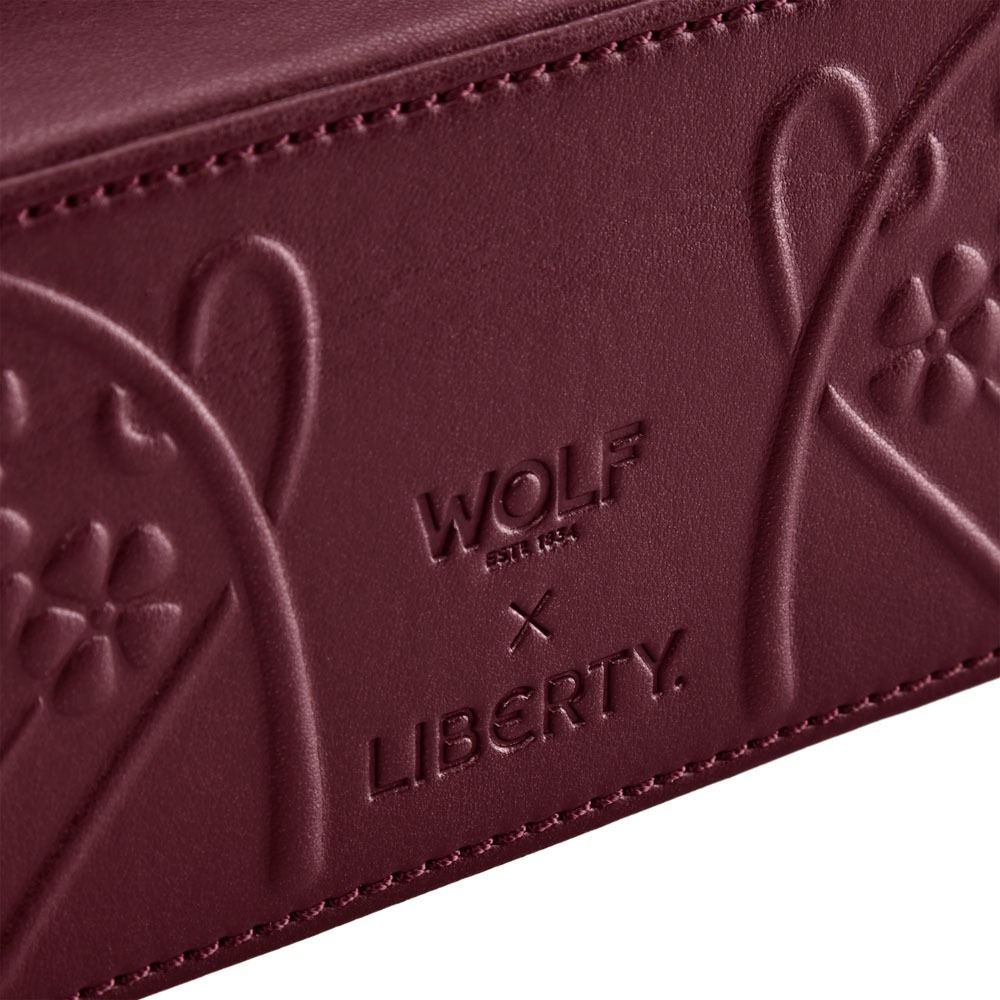 Close-up of maroon leather with embossed floral patterns and the words “WOLF EST. 1834 x LIBERTY,” highlighting the exquisite craftsmanship of the WOLF 1834 X Liberty All Over Ianthe Medium Jewellery Zip Case in Burgundy by WOLF.