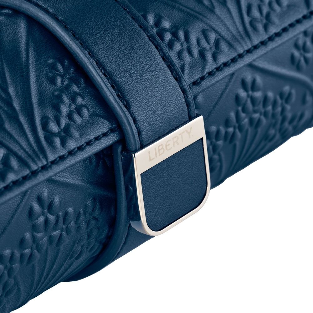 Close-up of the WOLF 1834 X Liberty All Over Ianthe Triple Watch Roll in Navy—crafted from blue leather with embossed floral patterns and a metal buckle engraved with “Liberty.” The elegant WOLF design evokes the craftsmanship of a luxury watch case, combining timeless style with dependable protection for your timepieces.