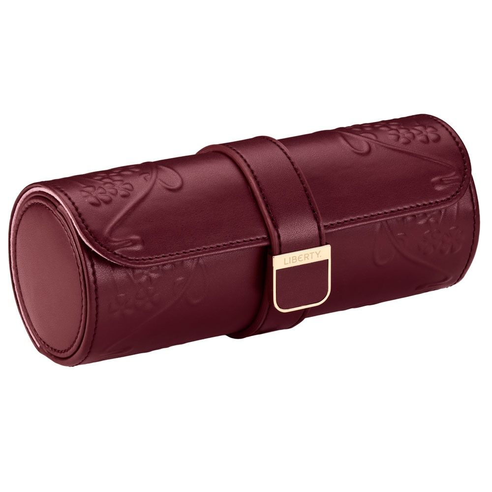 A cylindrical burgundy leather watch roll from WOLF, the WOLF 1834 X Liberty All Over Ianthe Triple Watch Roll, features embossed floral patterns and a gold clasp labeled “LIBERTY.” This elegant design not only showcases your timepieces but also offers a sophisticated storage solution for your treasured watches.