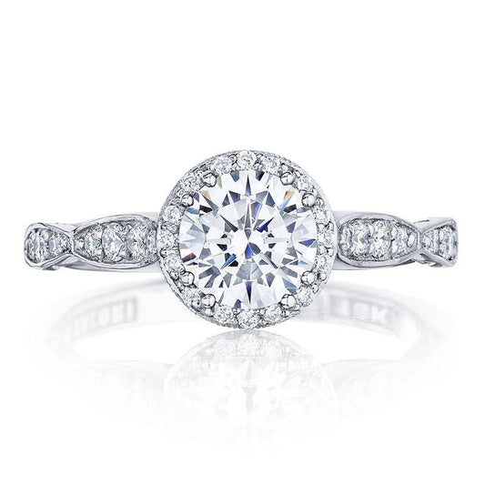 The Tacori Dantela 18K White Gold Round Brilliant Semi Mount Engagement Ring features a breathtaking centerpiece with a large round diamond surrounded by a radiant halo of smaller diamonds. The band, adorned with elegant diamond accents, is set on an impressive cathedral foundation.