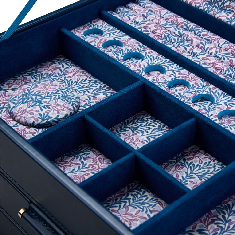 Close-up of the WOLF 1834 X Fiona Howard Sophia Jewellery Box With Drawers in Indigo Fruit Botanical, showcasing its blue leather exterior and multiple compartments lined with fabric featuring a purple and blue leafy botanical pattern.