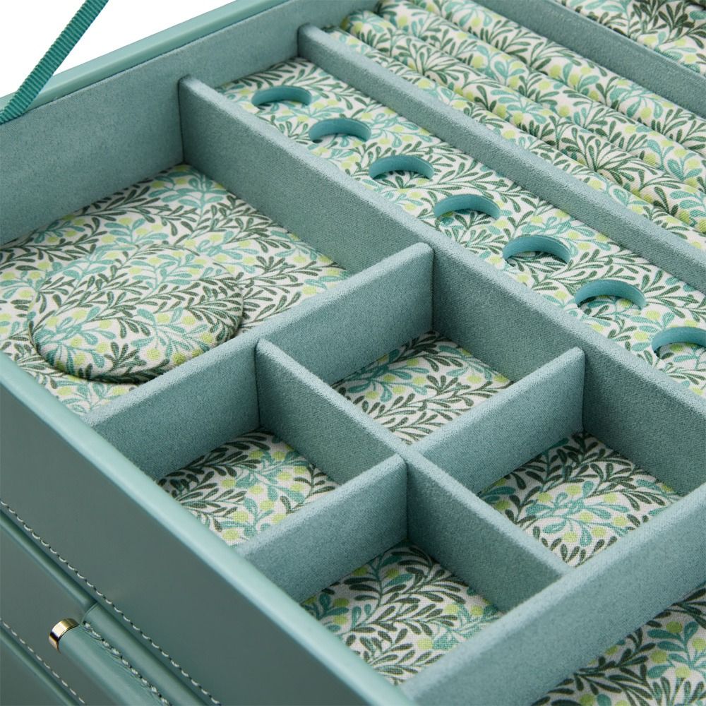 A close-up of the WOLF 1834 x Fiona Howard Sophia Jewellery Box With Drawers in Jade Fruit Botanical style, featuring multiple compartments lined with green, leafy-patterned anti-tarnish fabric. Some sections are empty, while others contain round and rectangular fabric pads. The soft teal exterior from WOLF adds a touch of elegance to this sophisticated jewellery box.