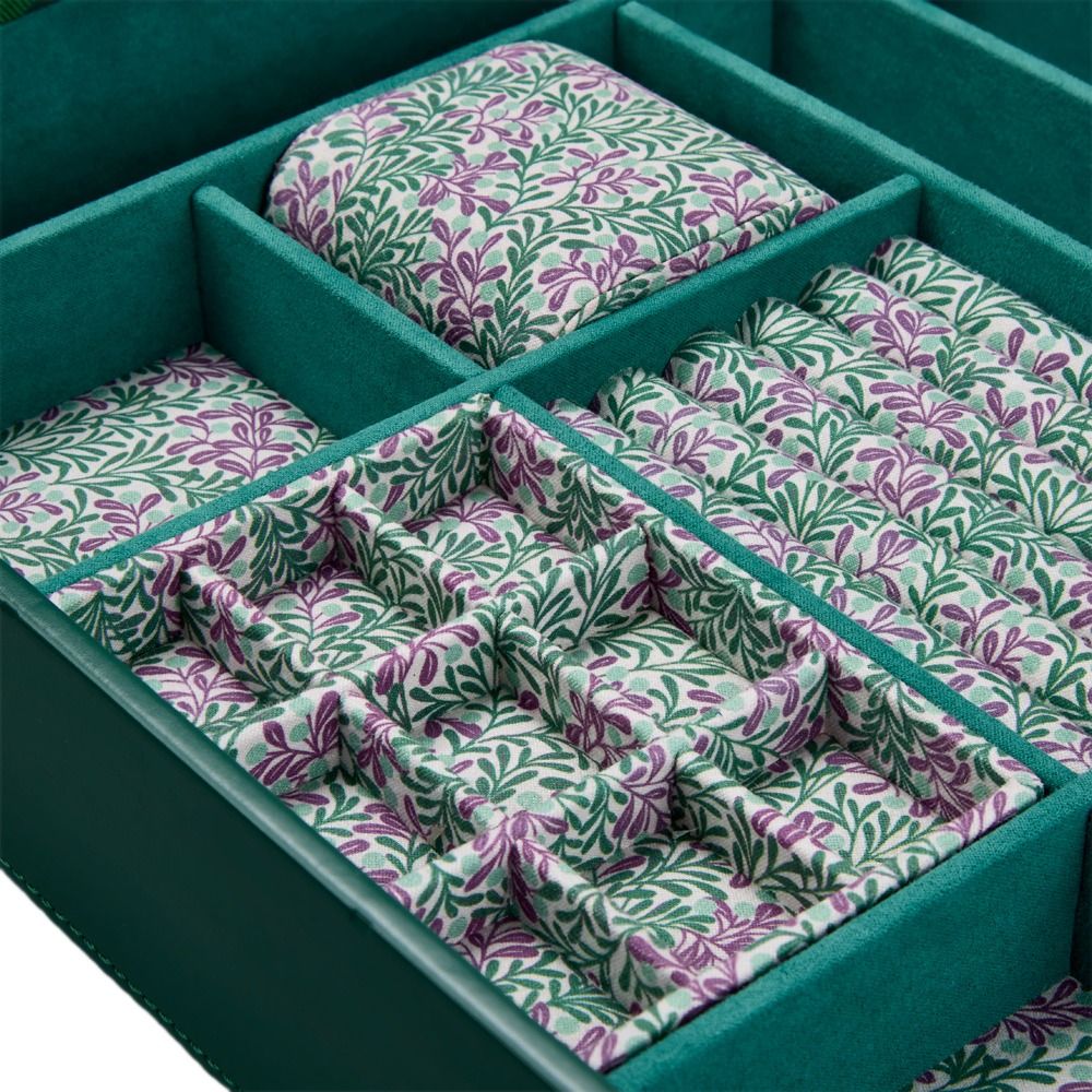 A close-up of the WOLF 1834 X Fiona Howard Botanical Jewellery Box With Window by WOLF, showcasing its green leather exterior and compartments lined with anti-tarnish fabric in a leafy pattern with purple berries. The interior features ring slots and padded sections for various jewelry pieces, making this elegant jewellery case both stylish and practical.