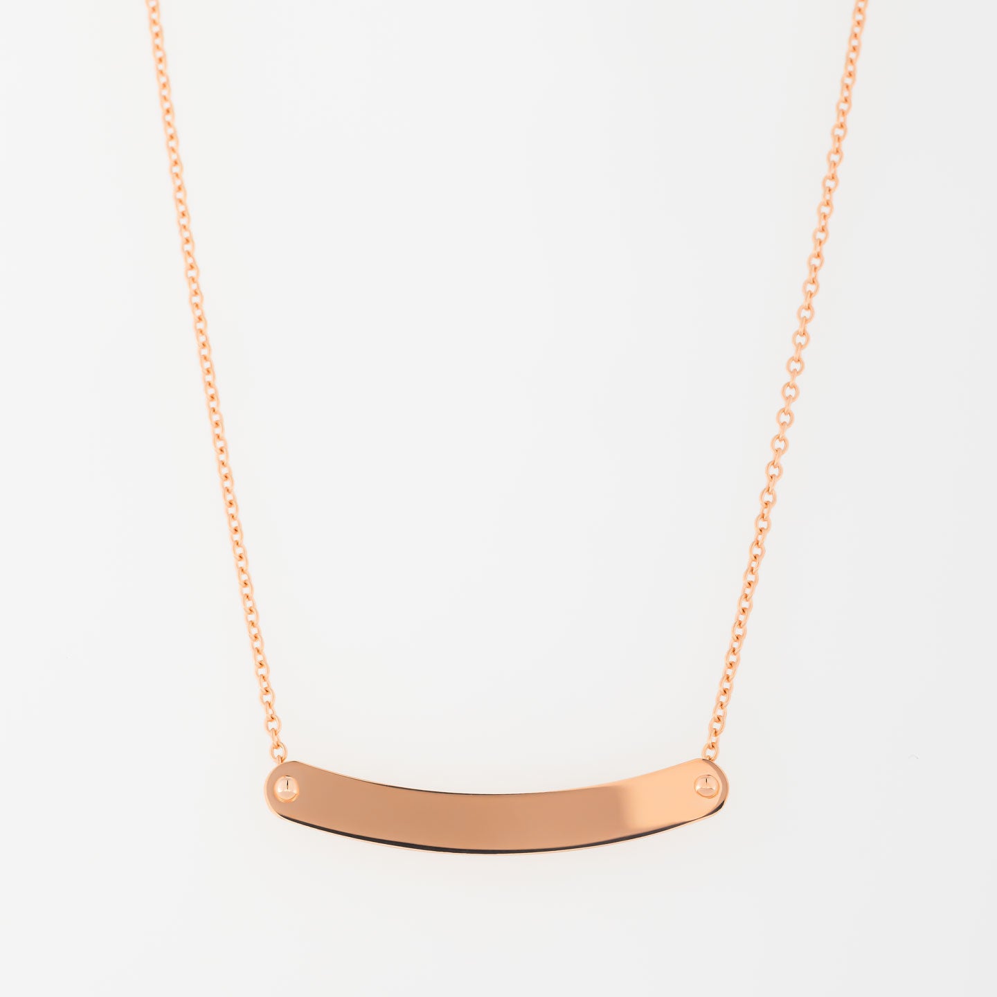 The Raffi&Co Rose Gold Engravable Necklace features an 18kt rose gold design with a simple chain and a curved horizontal bar pendant. Two small screws accentuate each end of the bar, all set against a plain white background. This elegant piece is sure to be a standout addition to your jewelry collection.