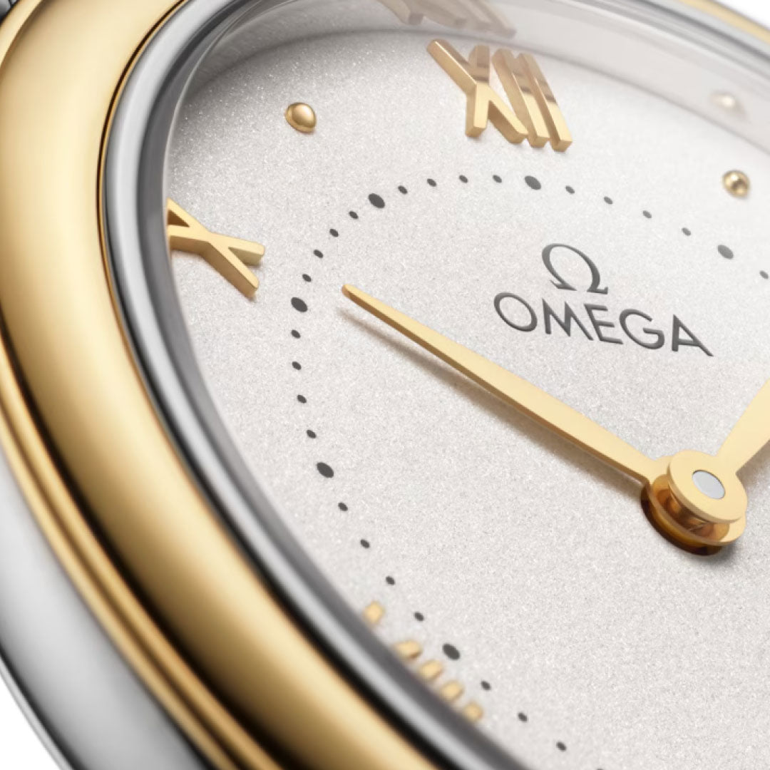 Close-up of the OMEGA De Ville Prestige Quartz 30mm Watch by OMEGA, featuring gold Roman numerals, a stainless steel and 18K yellow gold bezel, Omega logo on a textured light background, and gold minute and hour hands.