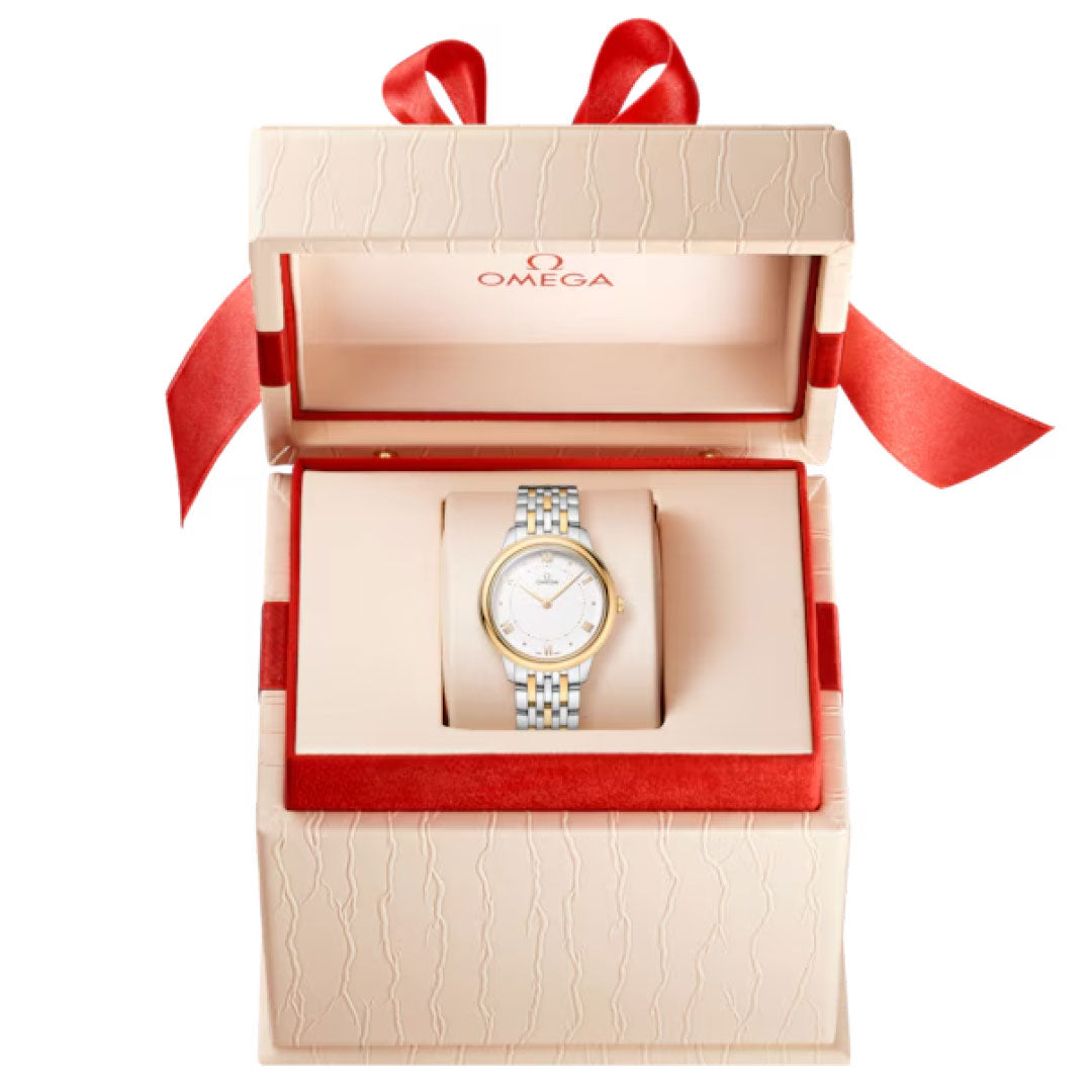An OMEGA De Ville Prestige Quartz 30mm watch in stainless steel and 18K yellow gold, featuring a white dial, presented in an open cream Omega box lined with red fabric and topped with a large red ribbon bow.