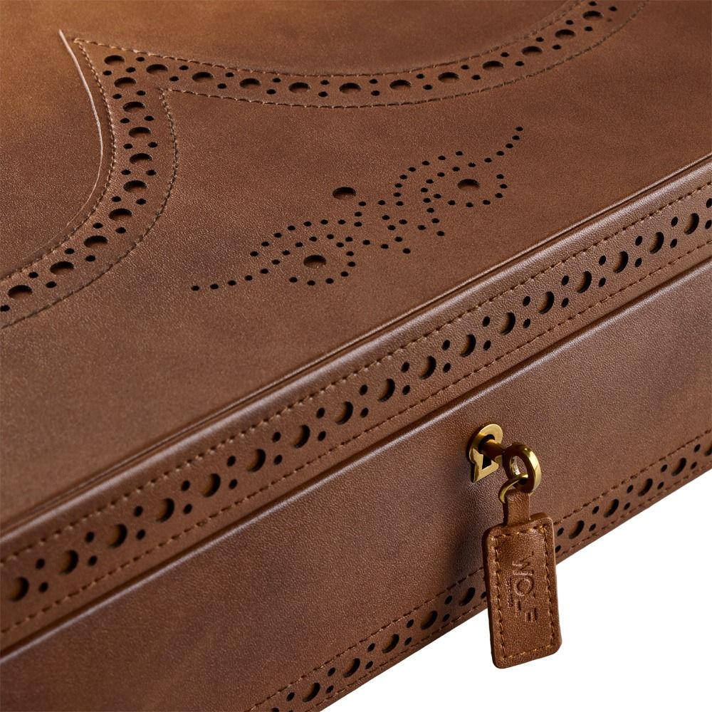 Close-up of the WOLF 1834 Brogue 10 Piece Watch Box in burnished brown vegan leather, showcasing decorative perforations, fine stitching, a small gold lock, and a leather tag embossed with the WOLF brand. This elegant accessory combines style and functionality, making it perfect for smart watch or watch storage.