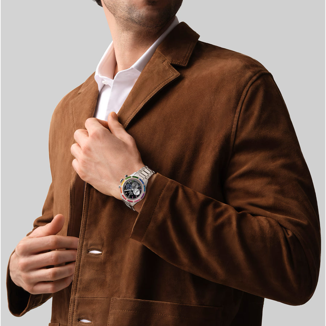 A person in a brown suede jacket and white shirt adjusts their collar, showcasing the ZENITH Chronomaster Sport El Primero 3600 41mm Watch by Zenith. This stunning silver timepiece features a detailed dark face and white gold casing, set against a plain light gray background.