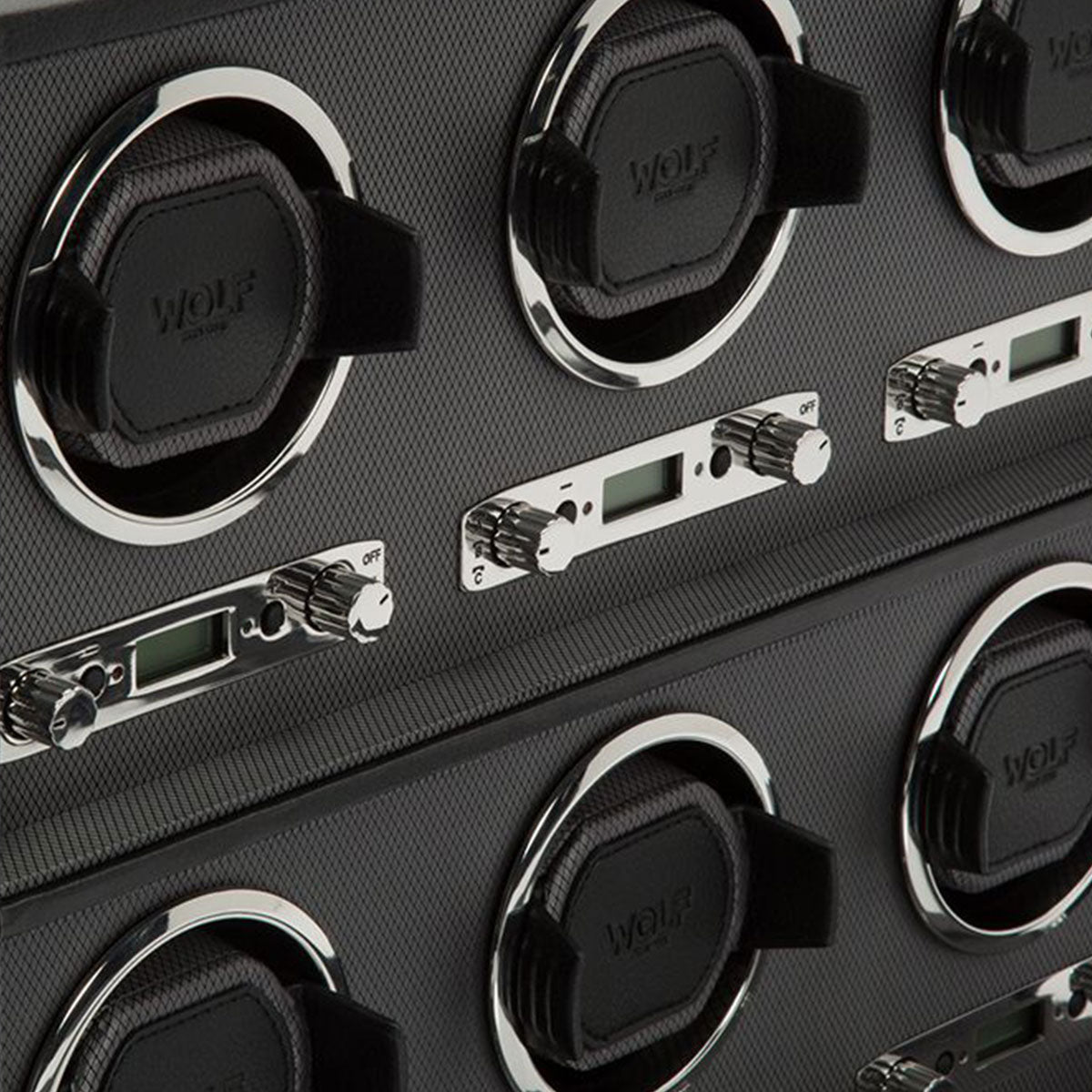 Close-up of a WOLF 1834 Viceroy 6 Piece Winder made from carbon fiber, featuring multiple padded watch holders with versatile rotation options. The control panels include digital displays and dials, while the brand name "WOLF" is embossed on the holders. Its sleek and modern design enhances its elegance.