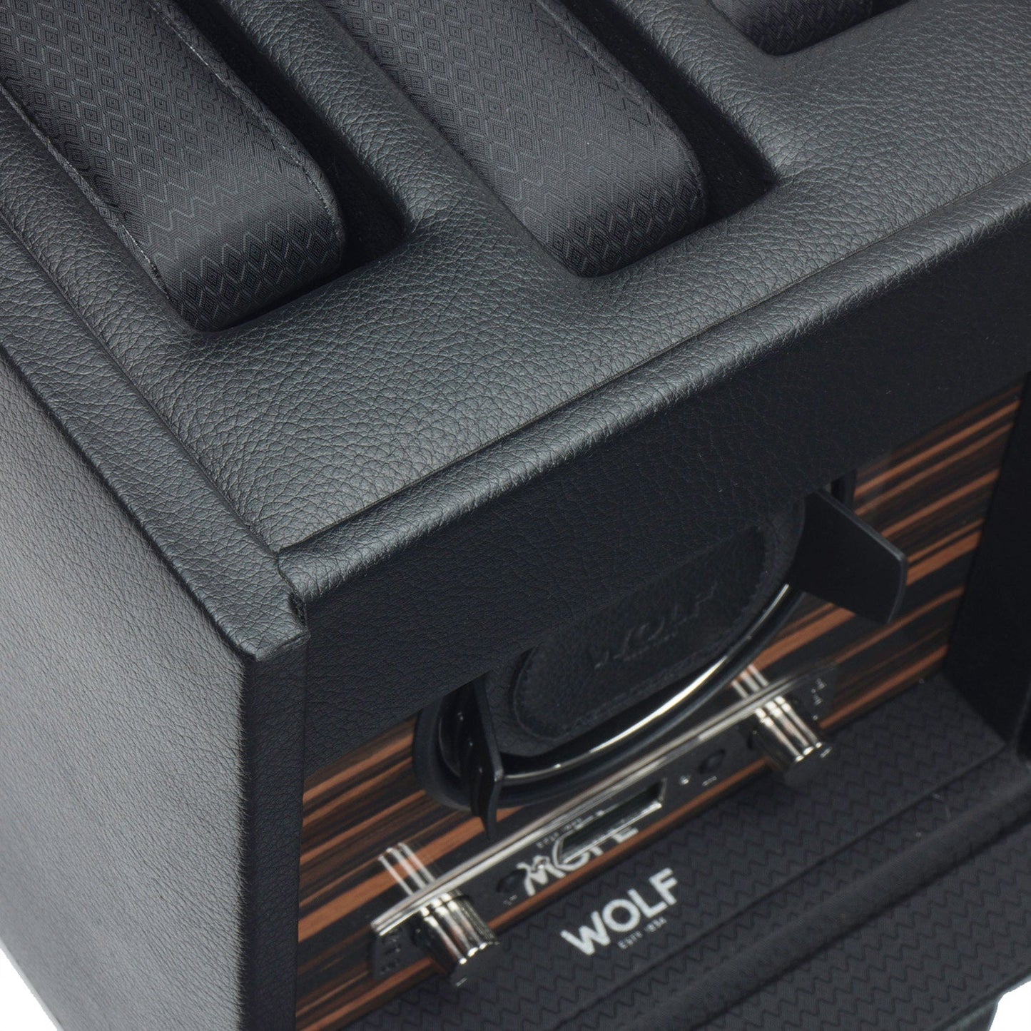 A detailed view of a WOLF 1834 Roadster Single Watch Winder With Storage in black vegan leather, showcasing its textured pattern. This innovative winder by WOLF includes multiple compartments, sleek metallic accents, a wood grain panel interior, and the brand name "WOLF" elegantly displayed inside.
