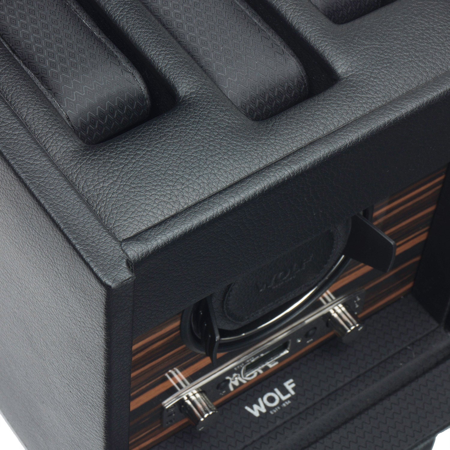 A detailed view of a WOLF 1834 Roadster Single Watch Winder With Storage in black vegan leather, showcasing its textured pattern. This innovative winder by WOLF includes multiple compartments, sleek metallic accents, a wood grain panel interior, and the brand name "WOLF" elegantly displayed inside.