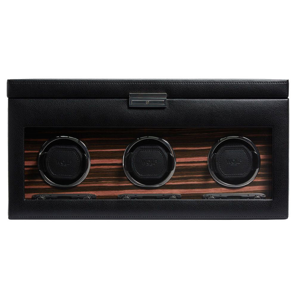 Introducing the WOLF 1834 Roadster Triple Watch Winder With Storage, a luxury accessory with a black leather exterior and a glass front, displaying three circular slots. This design is enhanced by an elegant wood-grain pattern and includes a dynamic cuff for secure fit. Additionally, it features a power reserve setting to ensure optimal performance of your timepieces.