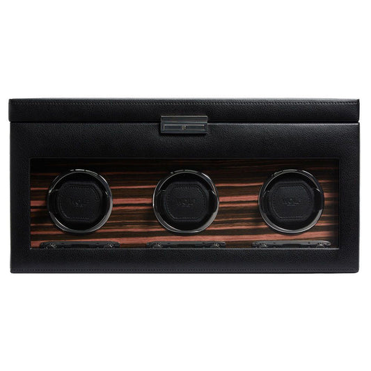 Introducing the WOLF 1834 Roadster Triple Watch Winder With Storage, a luxury accessory with a black leather exterior and a glass front, displaying three circular slots. This design is enhanced by an elegant wood-grain pattern and includes a dynamic cuff for secure fit. Additionally, it features a power reserve setting to ensure optimal performance of your timepieces.