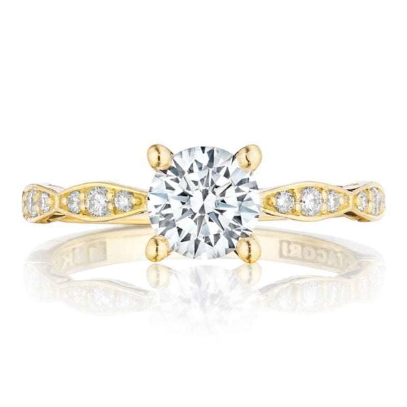 The Tacori Sculpted Crescent 18K Yellow Gold Round Brilliant Solitaire Semi Mount with Diamond Band Engagement Ring embodies elegance, featuring a large round diamond at the center. Its band, adorned with smaller diamonds in an alternating pattern, sparkles brilliantly on a white surface, capturing the timeless allure of exquisite engagement rings.