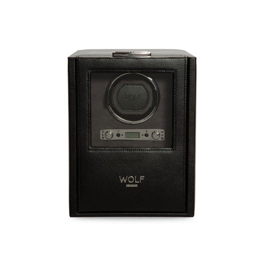 The WOLF 1834 Blake Single Watch Winder with Storage, crafted in black leather, boasts a transparent cover that reveals a circular slot for a watch. It includes a digital display and control buttons located below the slot, providing directional settings and rotation options. The brand name "WOLF" is prominently displayed on the front.